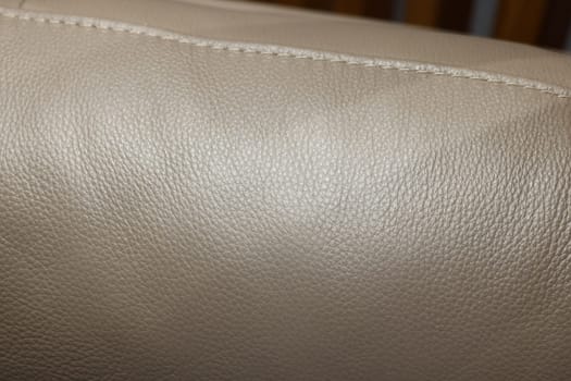Closeup view of a smooth, luxurious beige leather surface, highlighting its unique texture and stitching