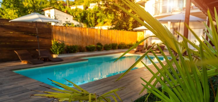 Swimming pool with wooden deck and green plants in sunlight. Concept of summer outdoor relaxation
