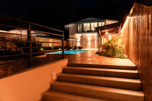 Modern villa entrance with illuminated stairs and swimming pool at night. Concept of elegant luxury property