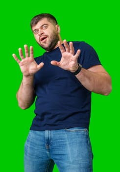 A man with a serious expression holds up both hands in a stopping gesture against a bright green background in studio
