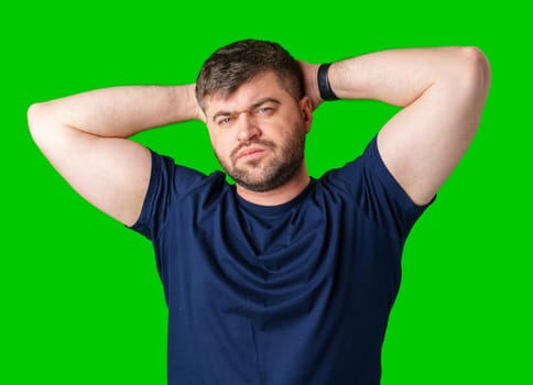 A man poses confidently with his hands behind his head against a bright green background in studio