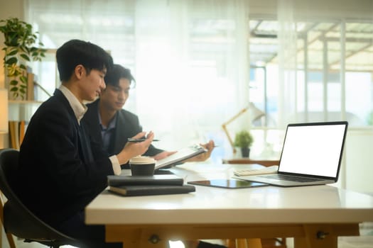 Laptop with a blank screen on white table with businessmen working together in bright office.