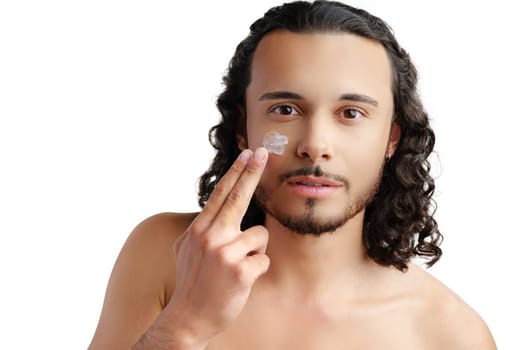 A young man demonstrates skincare routine with moisturizer on his face close up