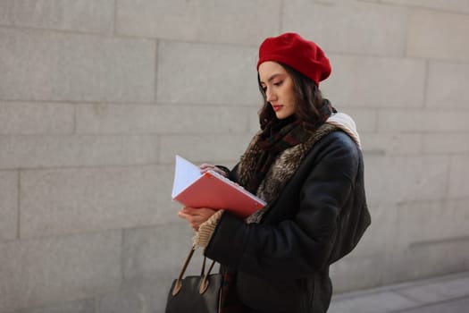 A stylish woman in a red beret jots down ideas while walking, highlighting her urban fashion and creativity