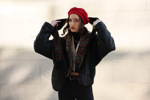 A woman exuding effortless style, donning a striking red beret, poses elegantly against an interesting, textured wall