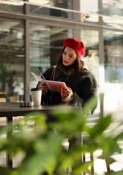 A stylish woman in a red beret reads notes while sipping coffee in a modern caf setting