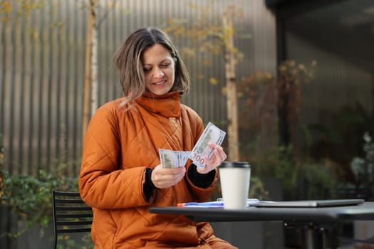A woman in an orange coat reads papers at an outdoor caf with a coffee cup