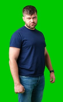 A determined young man stands confidently in casual attire against a bright green backdrop in studio