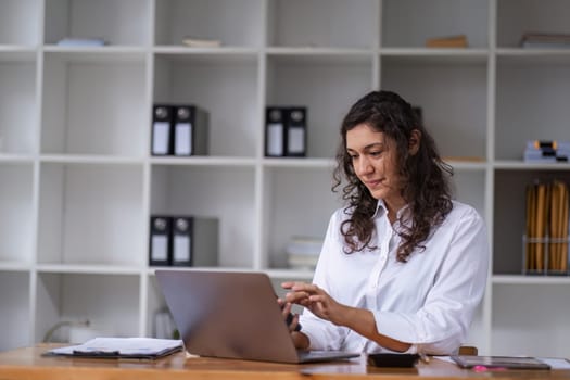 Professional businesswoman focused on work in a modern office setting, using a laptop at her desk.
