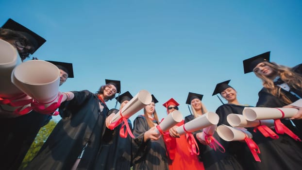 Group of students wearing graduation gowns and caps proudly showing their diplomas, celebrating their academic achievement