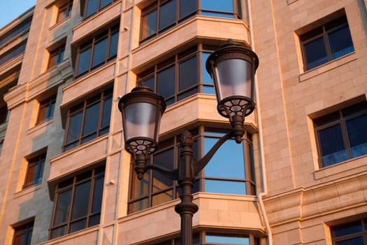 Street lamps are beautifully shining near modern contemporary buildings, creating a warm and inviting evening light
