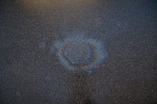 Iridescent gasoline spill forming a colorful circle on a wet asphalt surface