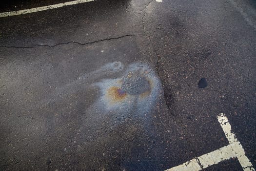 Gasoline or oil spill creating rainbow colors on wet asphalt parking lot surface.