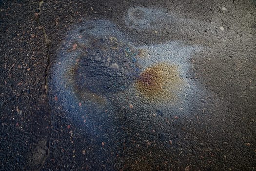 An iridescent gasoline leak creates a beautiful rainbow shine on asphalt, illustrating the impact of environmental pollution.