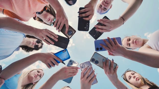 Group of young female friends taking photos with their mobile phones forming a circle with their devices against a blue sky