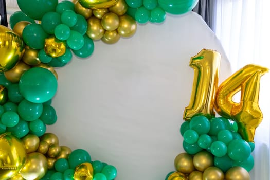 A vibrant balloon arch features green and gold hues, highlighting the number 14, perfect for a birthday celebration. The setup exudes a joyful atmosphere for the special occasion.