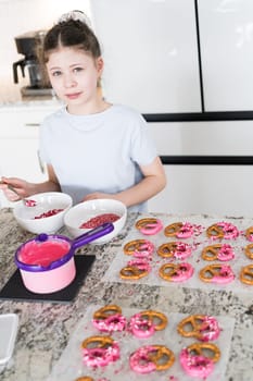 With focused attention, this budding culinary artist dips pretzels into a pot of melted chocolate, creating sweet delights in the warmth of a well-lit home kitchen.