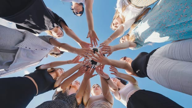 High school girls unite in a circle, holding a soccer ball together, demonstrating teamwork and solidarity against a clear blue sky