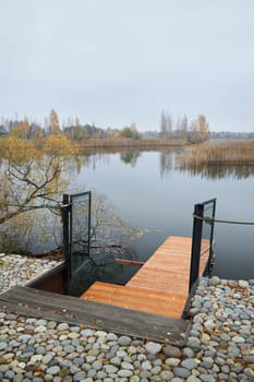 A serene wooden dock extends into a tranquil lake, framed by vibrant autumn trees and soft, muted skies