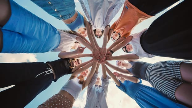 Group of young people forming a circle joining their hands together outdoors in a team building exercise