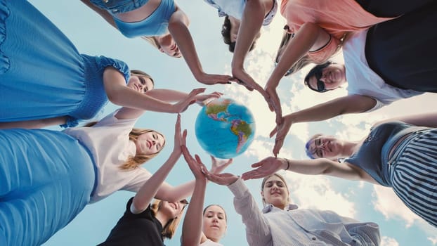 Group of young women forming a circle with their hands around a globe against a blue sky, symbolizing their commitment to environmental protection