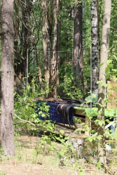 A neglected and abandoned piece of equipment lies partially concealed among the dense trees within a forest setting