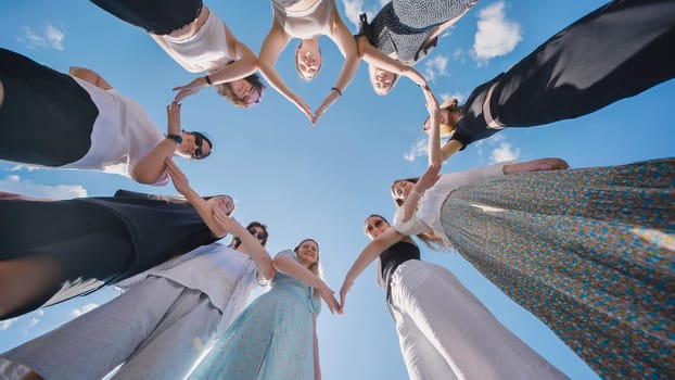 Group of high school students forming a circle with their hands against a blue sky, celebrating their friendship and unity during summer