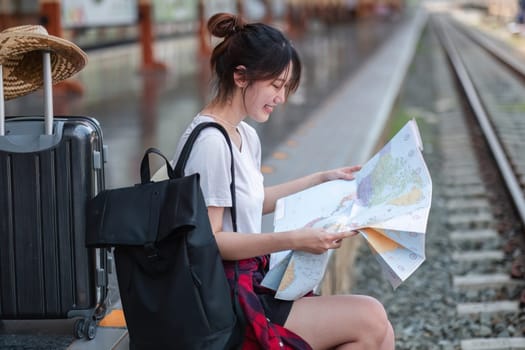 A cute young woman sits at a train station, looking at a map while waiting for the train. She is ready for an adventure and exploring new destinations.
