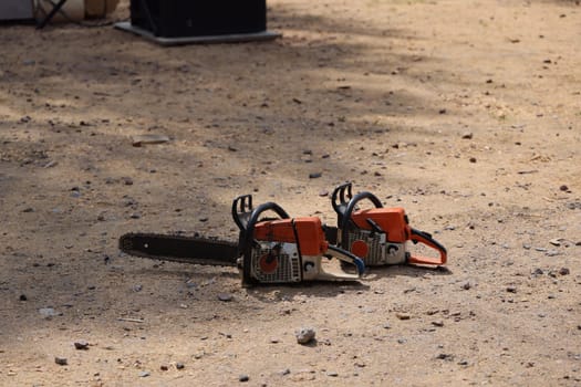 There are two chainsaws resting on a sandy surface, emphasizing outdoor tools and construction gear used
