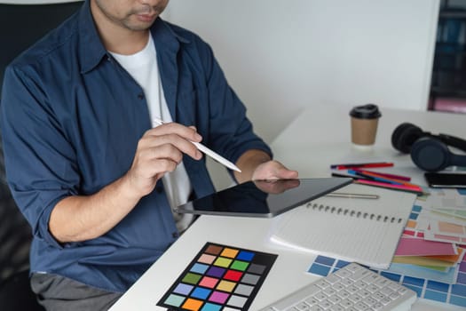 Graphic designer working on a project using a tablet and color swatches, showcasing creativity and planning in a modern office setting.