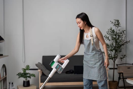 A young woman vacuums and cleans a modern living room, showcasing a minimalist and tidy home environment.