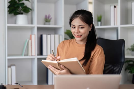 A young woman studying online at home, using a laptop and taking notes in a notebook, representing e-learning and remote education.