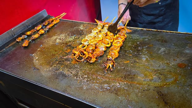 cook grills skewered squid over an open flame using a blowtorch, capturing the lively atmosphere of a bustling street food Thai market with bright flames and freshly prepared seafood.