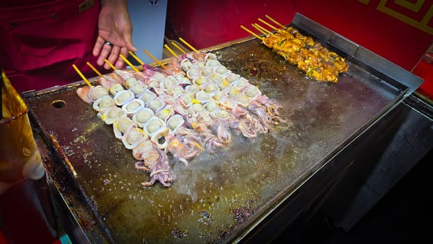 cook grills skewered squid over an open flame using a blowtorch, capturing the lively atmosphere of a bustling street food Thai market with bright flames and freshly prepared seafood.