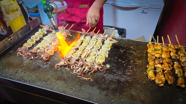 cook grills skewered squid over an open flame using a blowtorch, capturing the lively atmosphere of a bustling street food Thai market with bright flames and freshly prepared seafood.