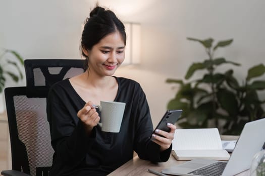 A young accountant working diligently on financial documents in a modern office, using a laptop and smartphone, with a cup of coffee and notebook nearby.