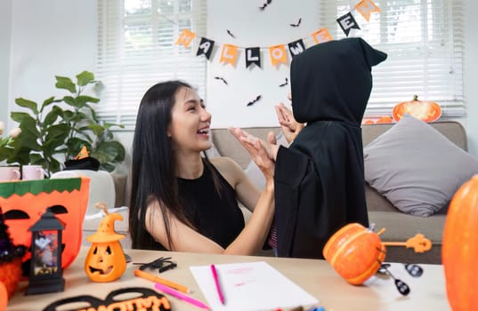 A joyful mother and daughter decorate their living room for Halloween, surrounded by festive decorations and costumes, creating a fun and spooky atmosphere.