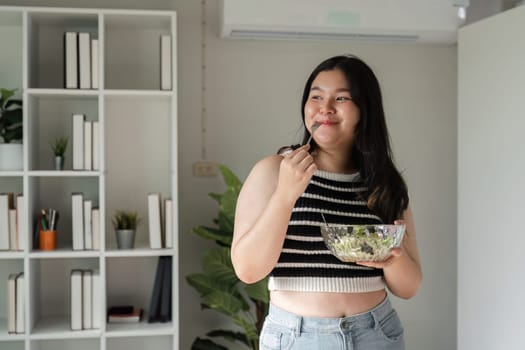 A young woman embraces a healthy lifestyle by enjoying a fresh vegetable salad in a modern home environment.