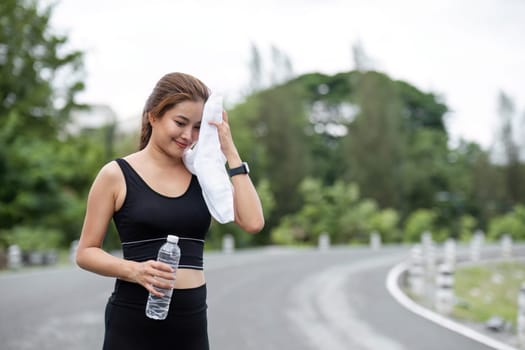 Young woman in athletic wear exercising at the park, holding a water bottle and towel, staying hydrated and healthy during her outdoor fitness routine.