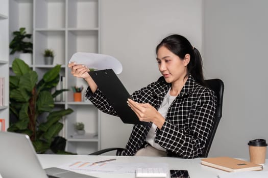 Professional office worker examining documents at a desk, surrounded by modern office supplies and greenery.