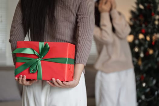A young woman surprises her partner with a gift on Christmas day, capturing a moment of joy and love in a festive home environment.