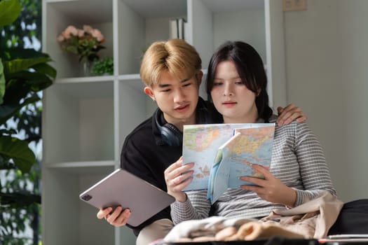 A young couple enthusiastically prepares for a vacation, surrounded by maps and travel gear in a cozy, modern home.