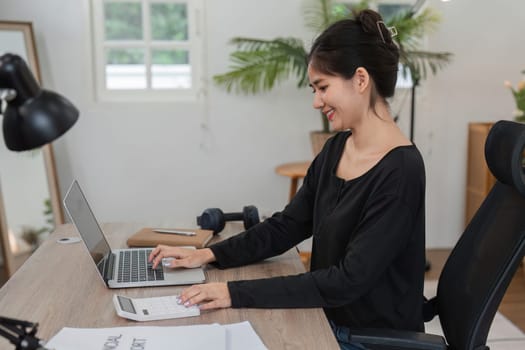 Woman planning her finances from home, working on a laptop and using a calculator in a modern home office environment.