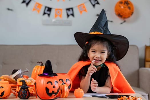 A cute young girl dressed in a Halloween costume, wearing a witch hat and surrounded by festive pumpkin decorations, smiling and enjoying the holiday.