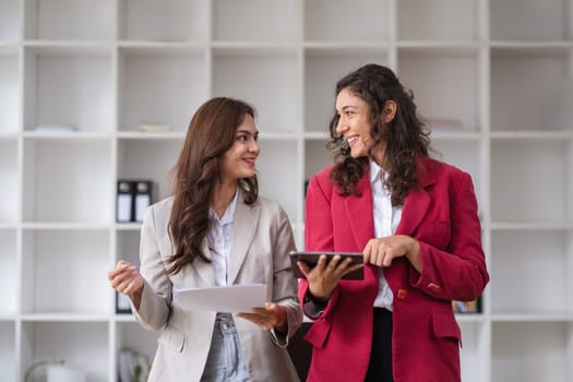 Two businesswomen engage in a collaborative discussion with colleagues, showcasing teamwork and professional consultation in a modern office setting.