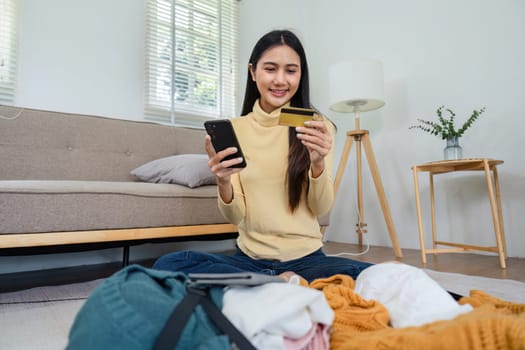 A young woman sits on the floor in a cozy living room, using her credit card and smartphone for online shopping.