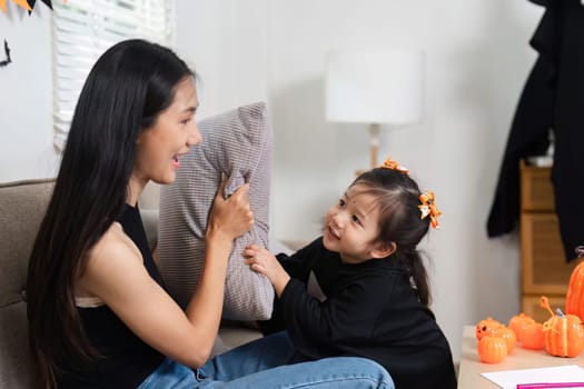 A loving mother and her daughter enjoy dressing up and decorating their living room for Halloween, creating a joyful and festive atmosphere.