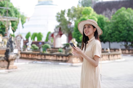 A young female tourist in a sun hat walks around a historic tourist attraction, holding a mobile phone and enjoying her travel experience.