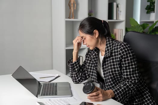 A young accountant experiencing stress while working at a desk with a laptop and coffee in a modern office setting.
