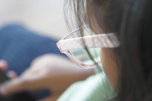 A young child wearing glasses is happily interacting with a smartphone device in a casual setting